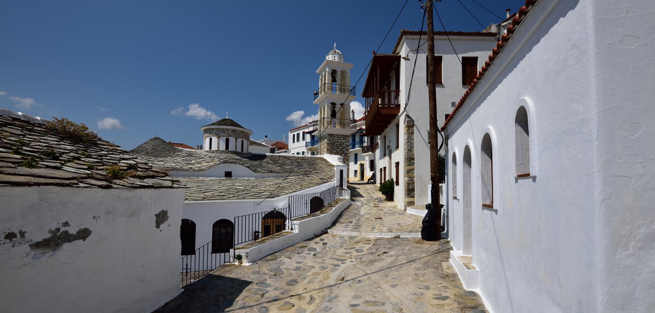White cobblestoned alley with a dominant church in the background in Skopelos, Greece
