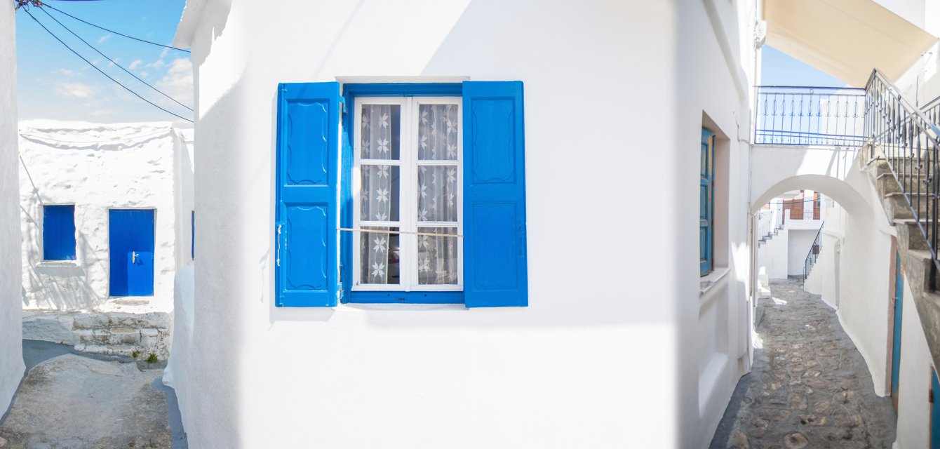 Front of a traditional island house with a blue window and bright white walls in Skyros, Greece
